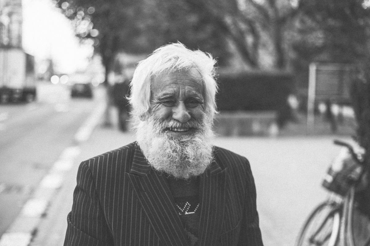 Elderly man wearing a chalkstripe peaked lapel jacket and smiling in B&W