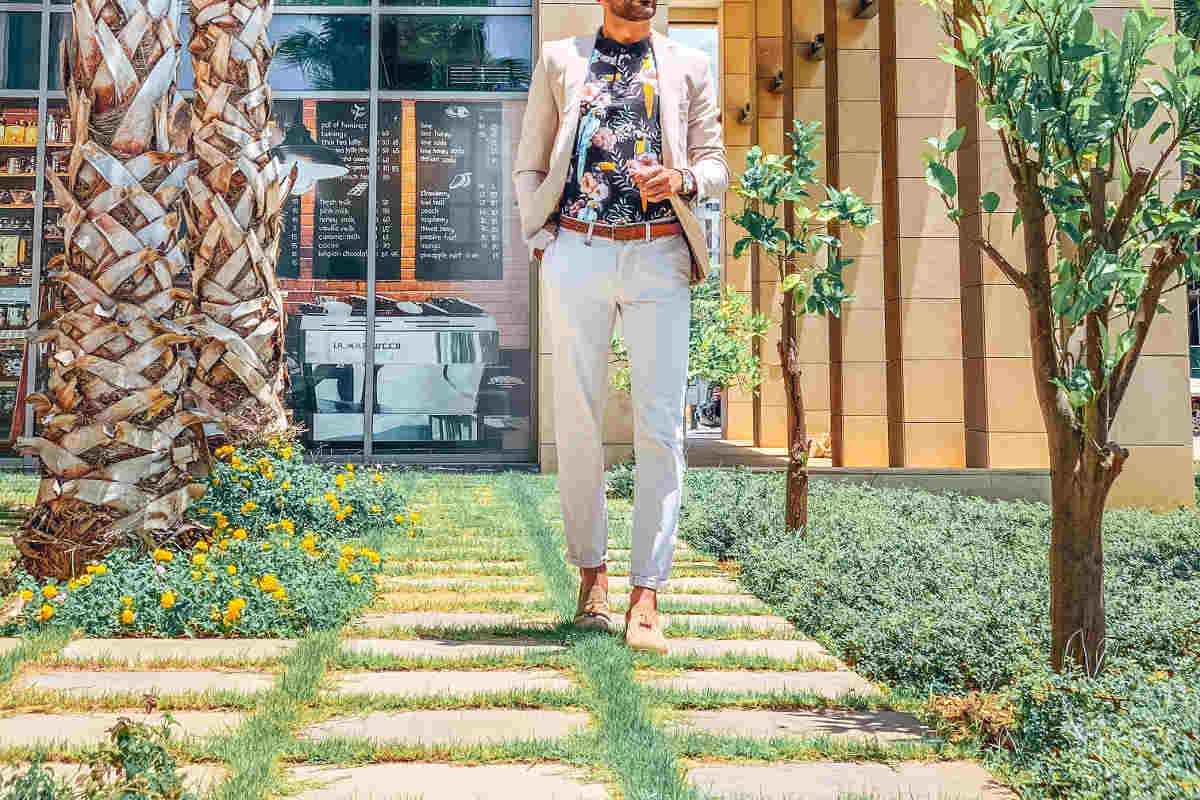Gentleman wearing off-white slacks, cotton sports coat and floral shirt walking on a garden