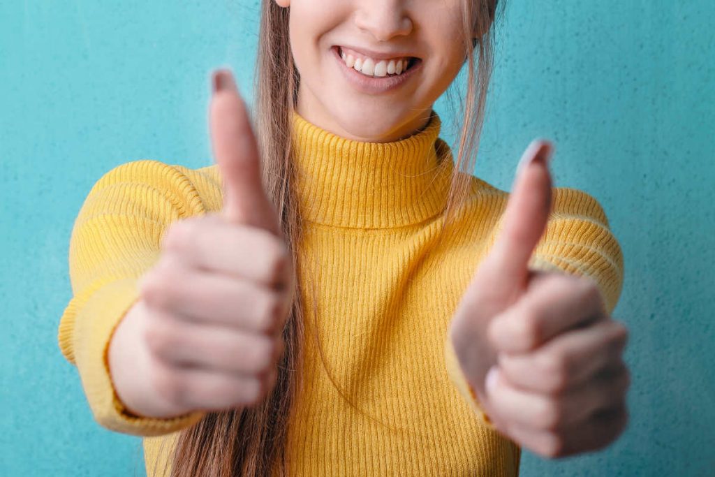 Girl wearing a yellow turtleneck sweater smiling and giving two thumbs up