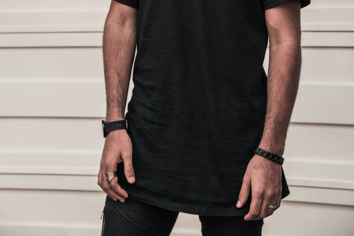 Close up to a men's hips wearing a long t-shirt over denim pants