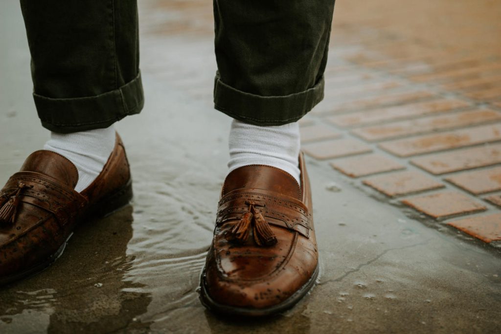 Close up of tassel loafers worn with white socks and green denim pants