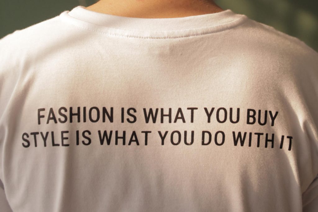 Person's back with a white t-shirt written Fashion is what you buy Style is what you do with it