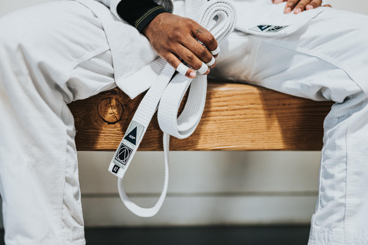 Close up on someone's hand holding a white martial arts belt between their legs