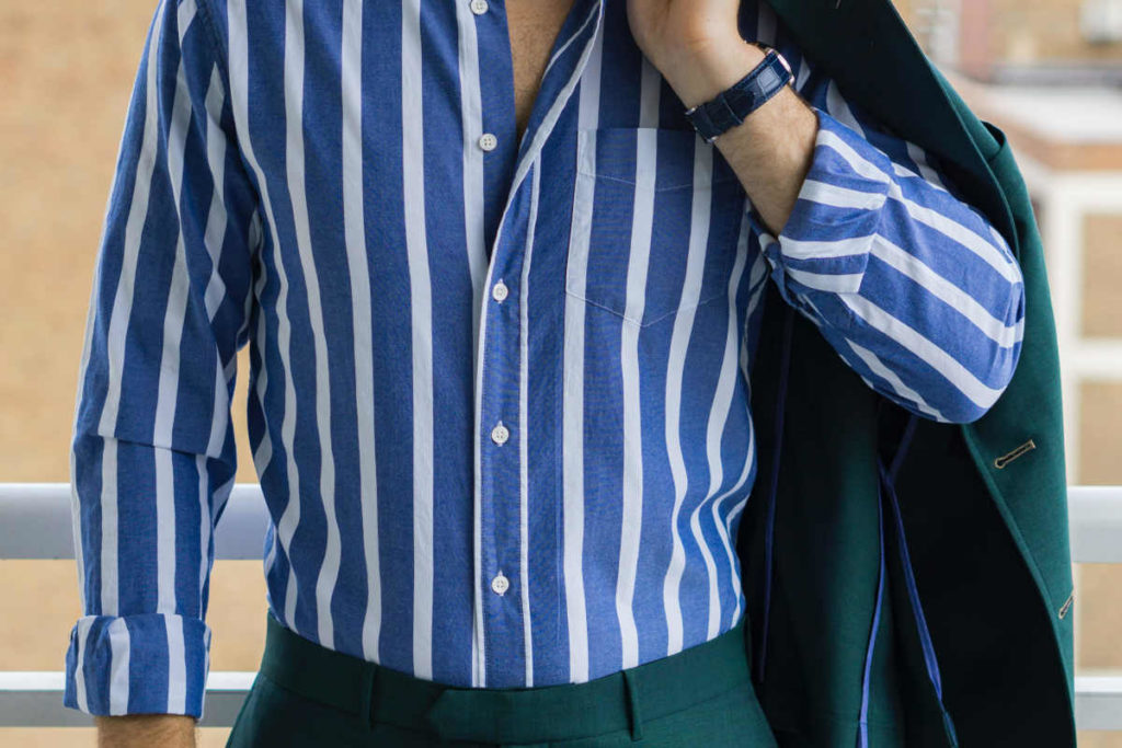 Close up of a man's torso wearing an emerald green suit with a white on blue madras stripe shirt