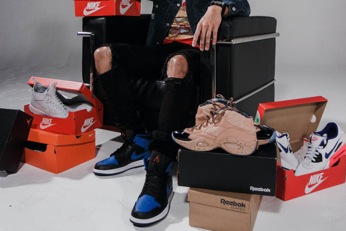 Waist down shot of a young man sitting on a chair surrounded by brand name sneakers