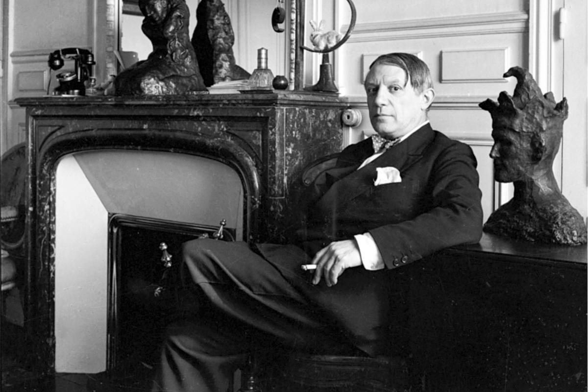 Pablo Picasso sitting on a chair in his study, wearing a two piece suit with a bow tie