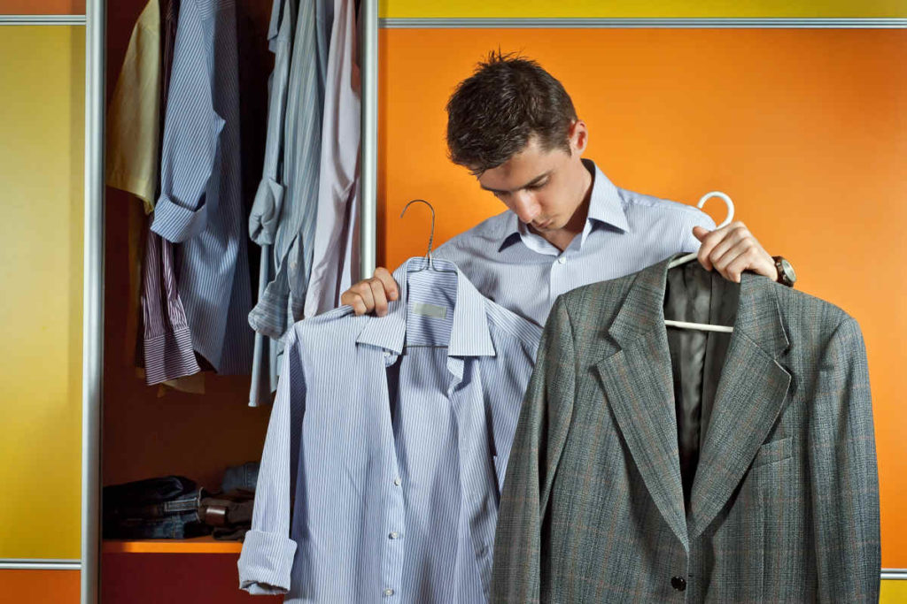 A man in a striped shirt tries clothes on the background of the closet. Yellow and orange wardrobe. The guy picks up the suit. The concept of clothing selection problem.