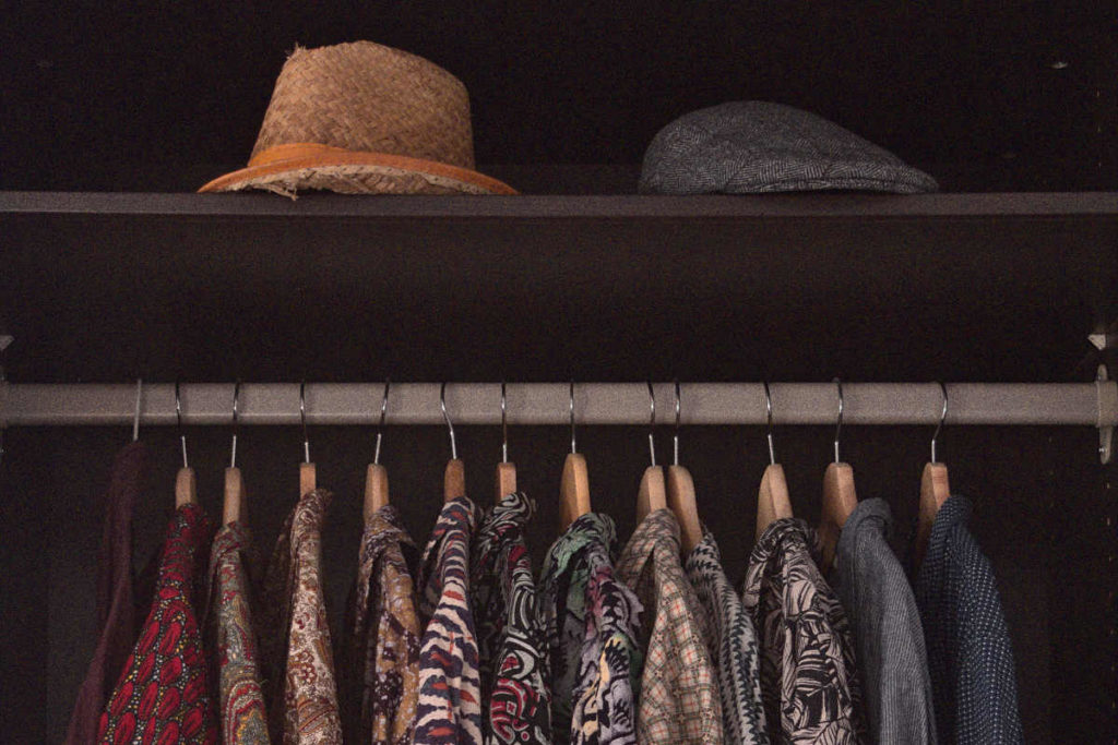 Wardrobe inside with colourful shirts hanging and two hats on the top drawer