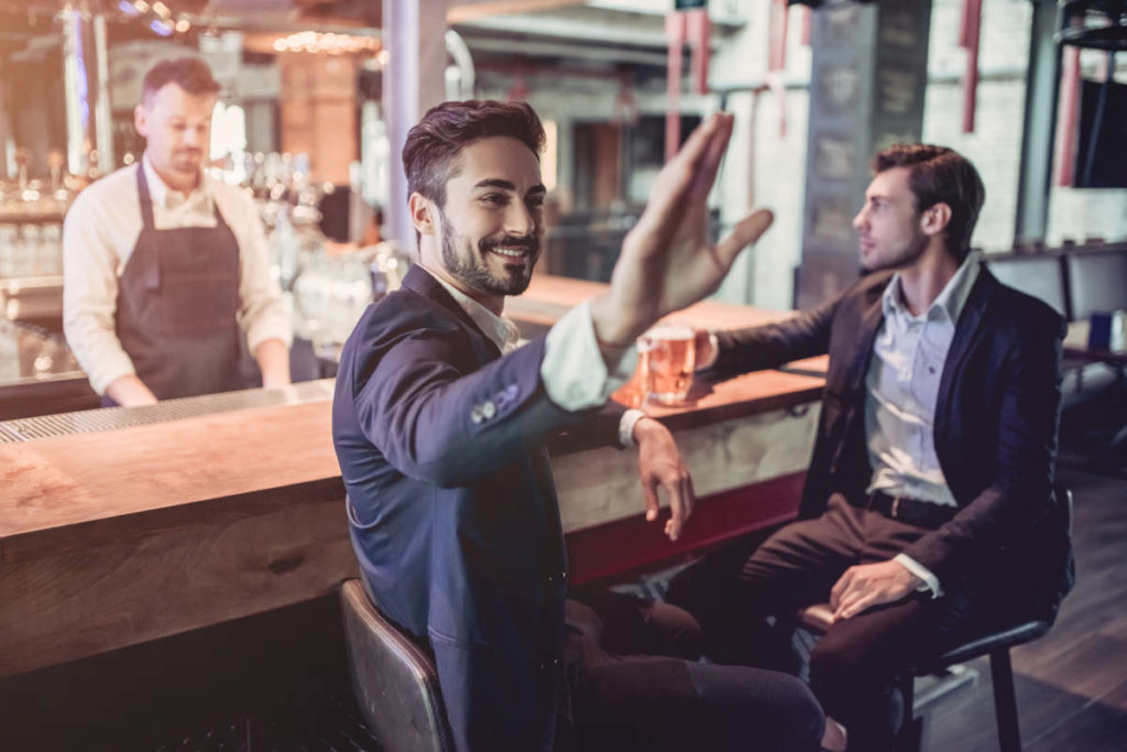 Handsome businessmen are sitting on a bar counter, drinking beer and looking for a waiter.
